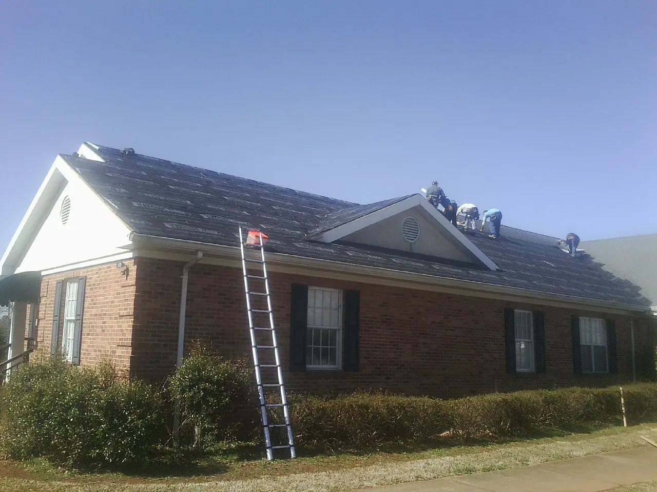 Crew tearing shingles off a brick ranch roof with a ladder set — Metal Roof Repair work by our crew in Dover